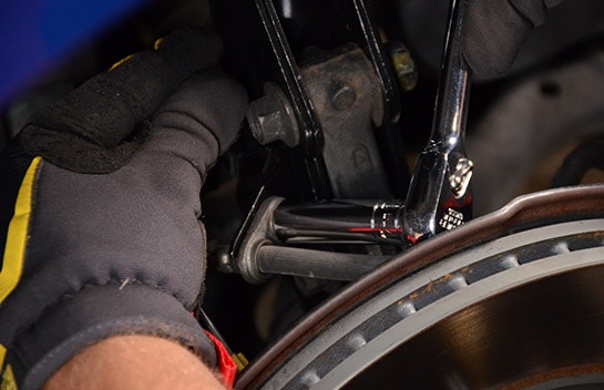 Close up image of a socket wrench reinstalling the brake hose bracket