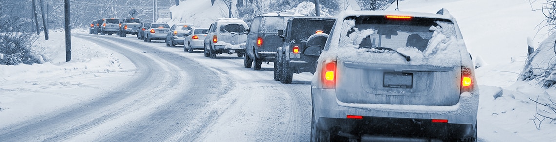 A lane of vehicles driving on a road thick with snow.