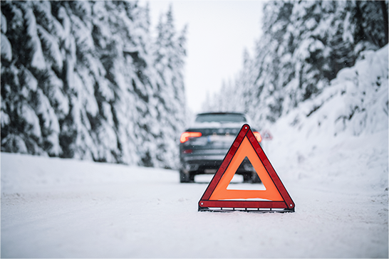 A triangular, orange and red safety cone sitting in the middle of a road covered in snow.