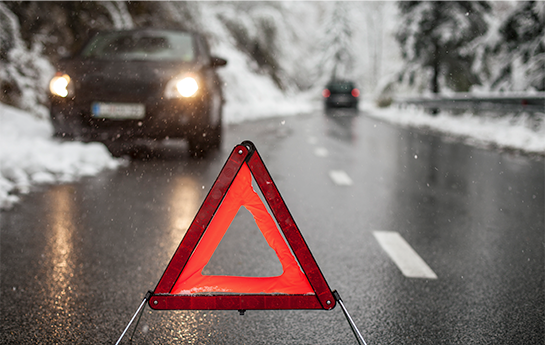 An triangular, orange and red safety cone sitting in the middle of a road with snow piled on the sides.