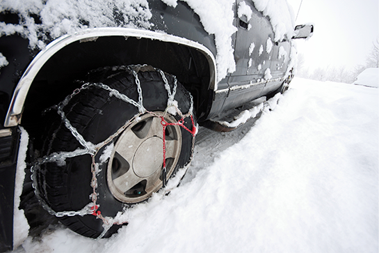 A vehicle driving through snow with chains wrapped around its tires.