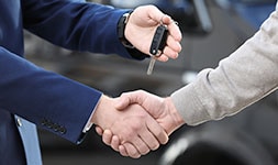 Two people shake hands, while another hand extends holding a set of car keys.