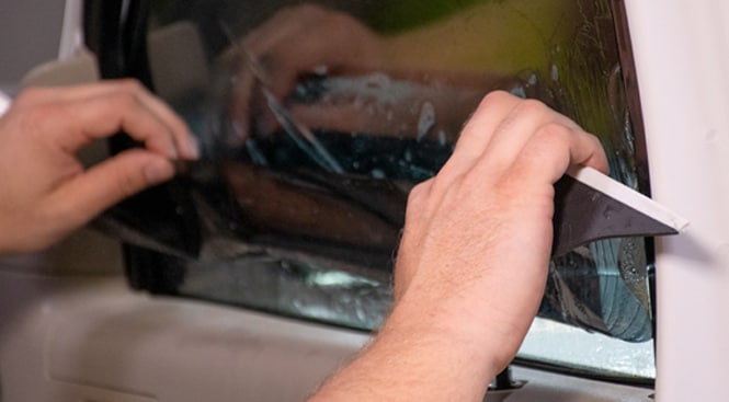 To ensure the bottom of the glass is clean, respray and squeegee the window. Wet the window again, then unfold the film onto the glass. Slip the bottom of the film under the gasket.