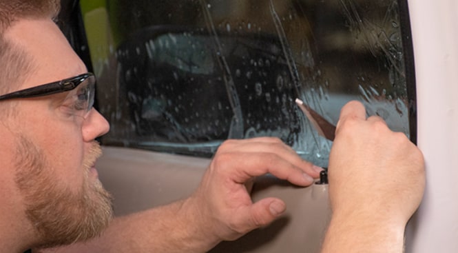 Carefully using the hard edge of the squeegee to slide the film behing the gasket.