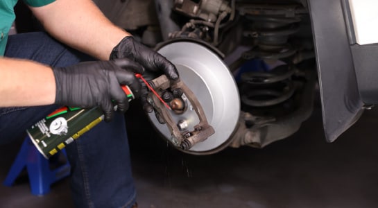 Brake cleaner is sprayed on the caliper bracket.
