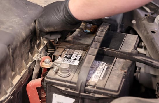 Using a ratchet and deep 10mm socket to loosen and removing the fasteners securing the battery hold-down.