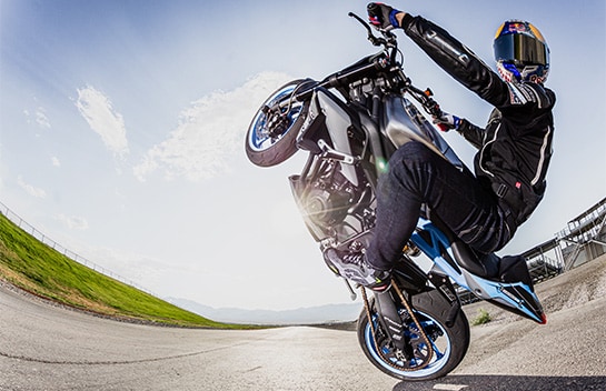A rider performing a wheelie on a motorcycle, captured by a fisheye camera lens
