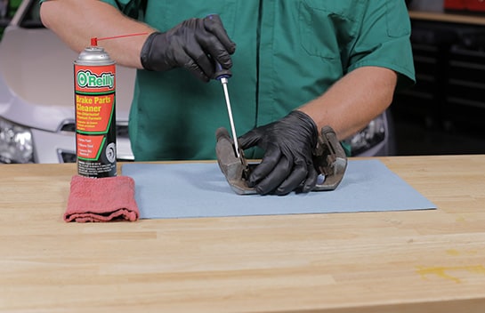 Use a flathead screwdriver to remove the old hardware from the caliper bracket. 