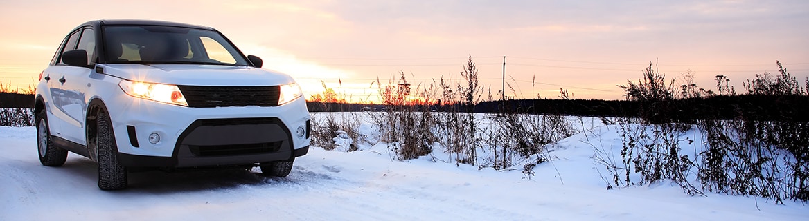 White SUV driving on a snowy, winter road under a sunset