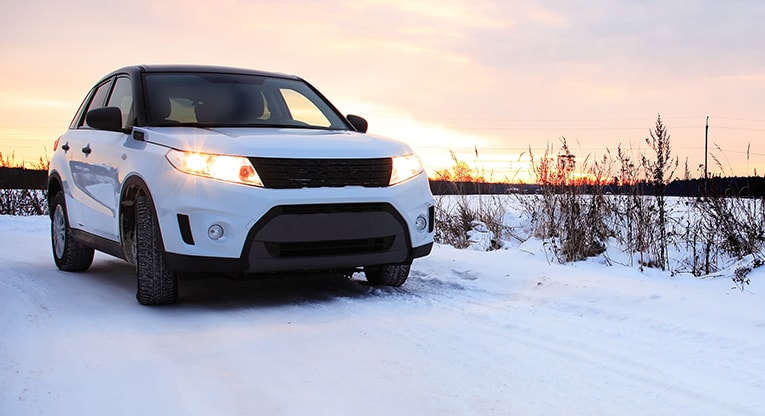 White SUV driving on a snowy, winter road under a sunset