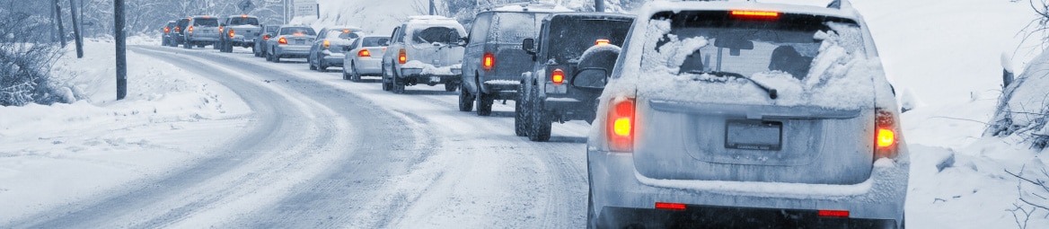 A lane of vehicles driving on a road thick with snow.