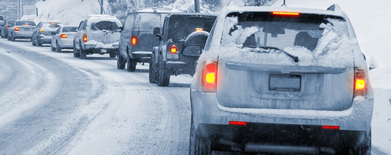 A lane of vehicles driving on a road thick with snow.