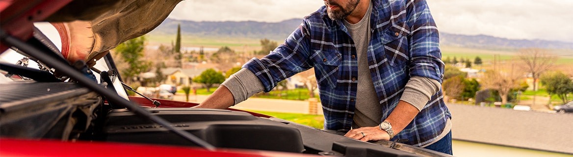 Man inspecting a car engine under the hood while troubleshooting possible starter issues.