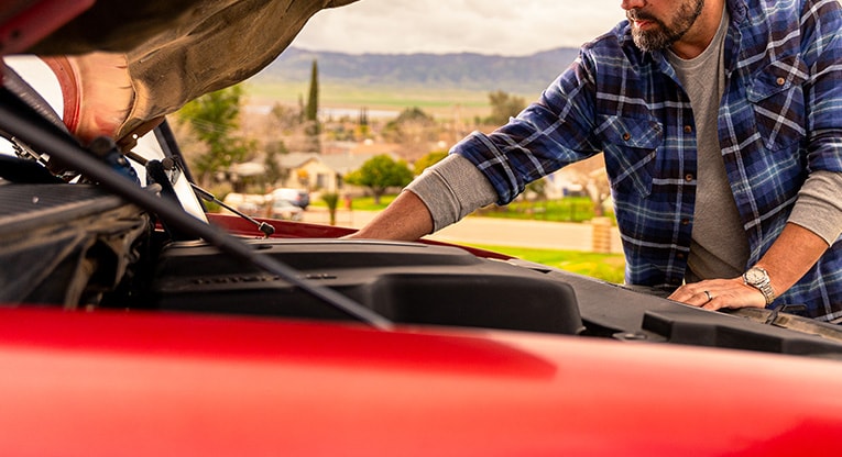 Man inspecting a car engine under the hood while troubleshooting possible starter issues.