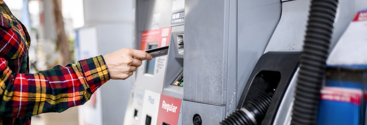 A person at a gas station pump inserting their credit card into the pump with the handle still docked.