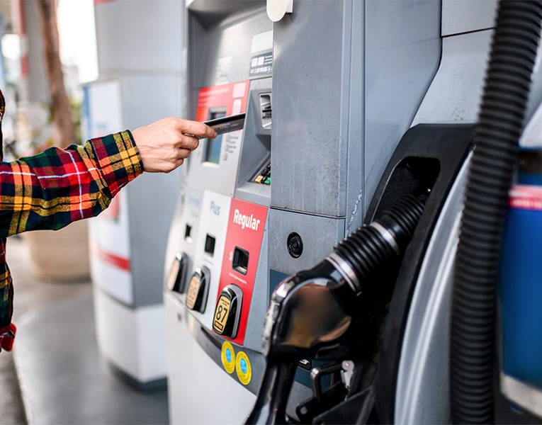 A person at a gas station pump inserting their credit card into the pump with the handle still docked.