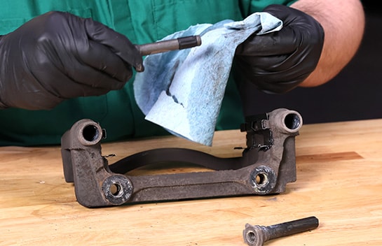 Auto parts professional reinstalling the slide pins on a caliper bracket