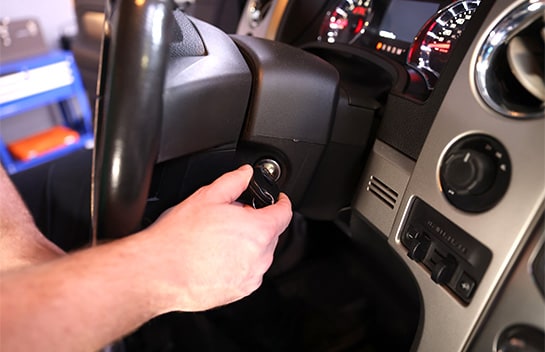 A driver attempting to turn the ignition key in a vehicle's steering column, experiencing a car won't start due to a bad starter solenoid or ignition switch failure.