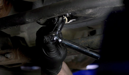 Auto parts professional reinstalling a drain plug on a Ford F-150