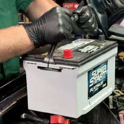 gloved hands putting in a new super start battery