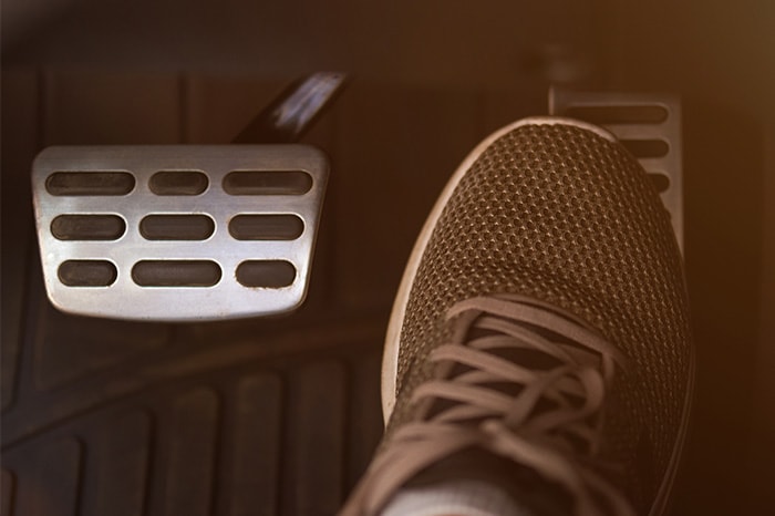 A person wearing athletic shoes hovers their right foot over a vehicle’s brake pedal.